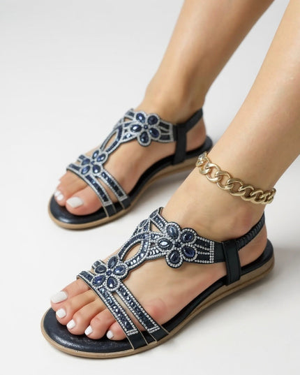 Black flat sandals with crystal-embellished straps and flower motifs worn on feet