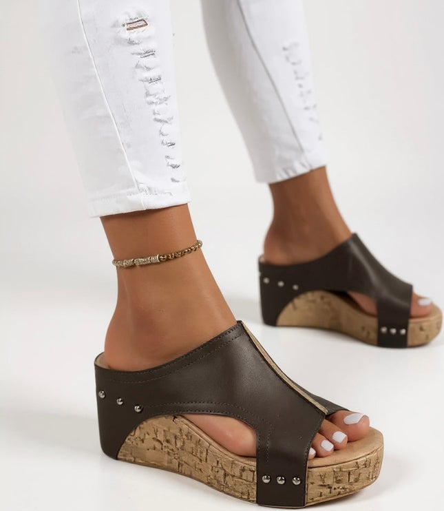 Side profile of black wedge slide sandal with metallic studs and textured cork heel