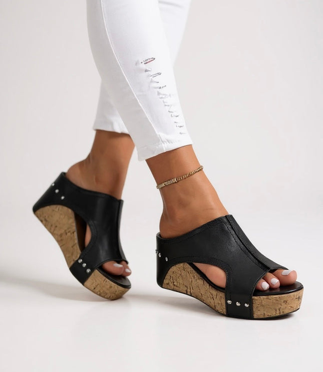 Black leather wedge slide sandals with silver studs and cork sole worn on feet