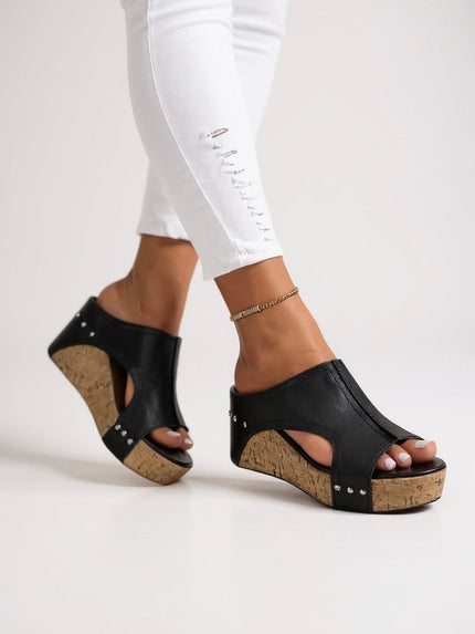 Black leather wedge slide sandals with silver studs and cork sole worn on feet