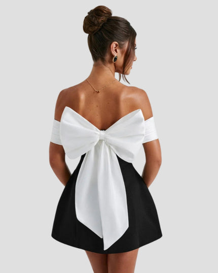 Back view of black mini dress with large white bow detail and off-shoulder design