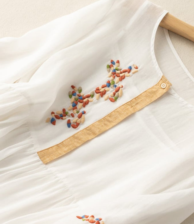 Close-up of white embroidered midi dress with multicolor floral stitching and tan placket