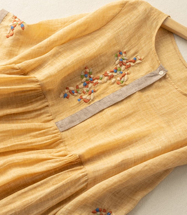 Close-up of mustard yellow embroidered midi dress showing floral chest detail and sleeve trim