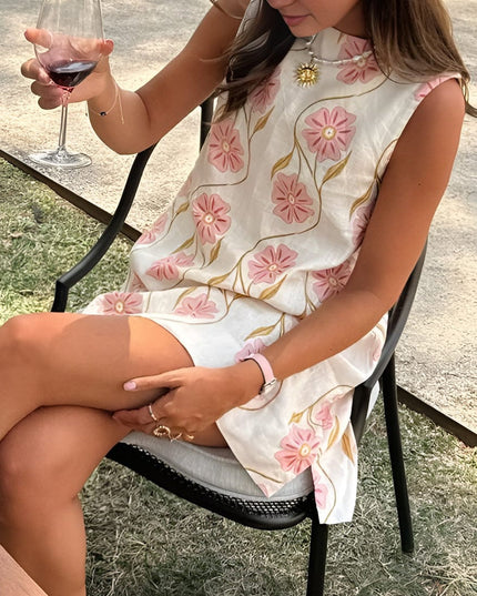 Women's summer floral sleeveless mini dress shown seated, with pink blossoms and a relaxed loose fit