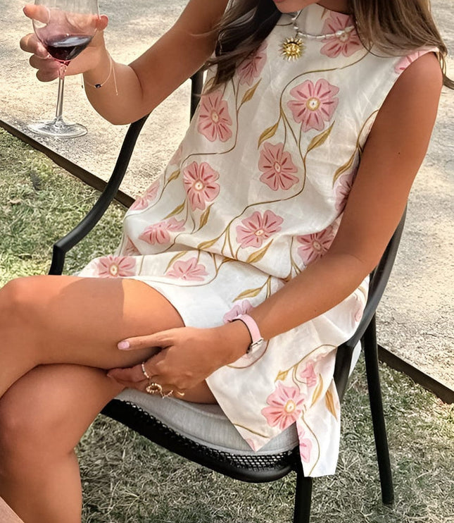 Women's summer floral sleeveless mini dress shown seated, with pink blossoms and a relaxed loose fit