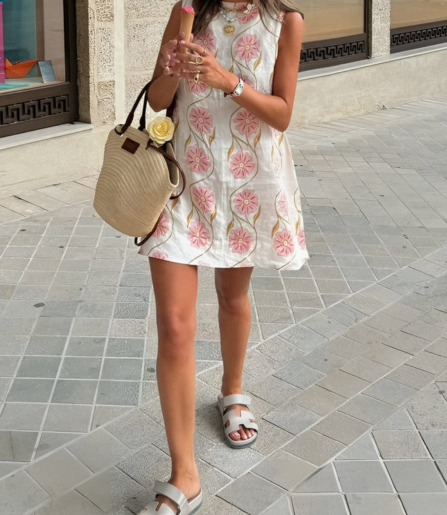 Front view of a sleeveless summer dress with pink floral print, styled with a straw tote and sandals