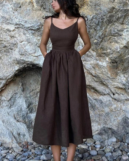 Dark brown linen maxi dress with spaghetti straps and full gathered skirt against rock wall