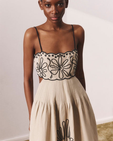 Close-up front view of beige midi dress with black floral embroidery and pleated waist