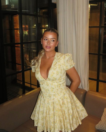 Yellow floral V neck mini dress with puff sleeves and flared skirt in indoor lounge setting