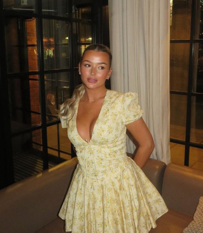 Yellow floral V neck mini dress with puff sleeves and flared skirt in indoor lounge setting