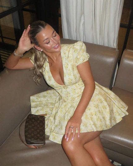 Woman seated in a yellow floral summer dress with V neck, puff sleeves, and mini length