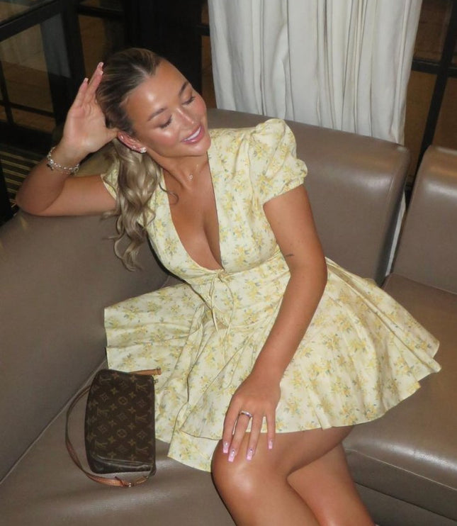 Woman seated in a yellow floral summer dress with V neck, puff sleeves, and mini length