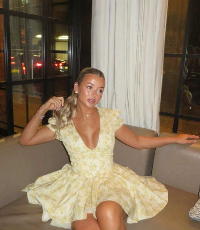 Yellow floral V neck mini dress with puff sleeves and gathered waist shown in a seated pose