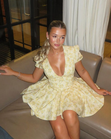 Close seated view of a yellow floral mini dress with deep V neck, puff sleeves, and full skirt