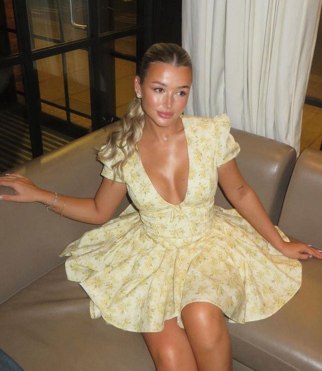 Close seated view of a yellow floral mini dress with deep V neck, puff sleeves, and full skirt