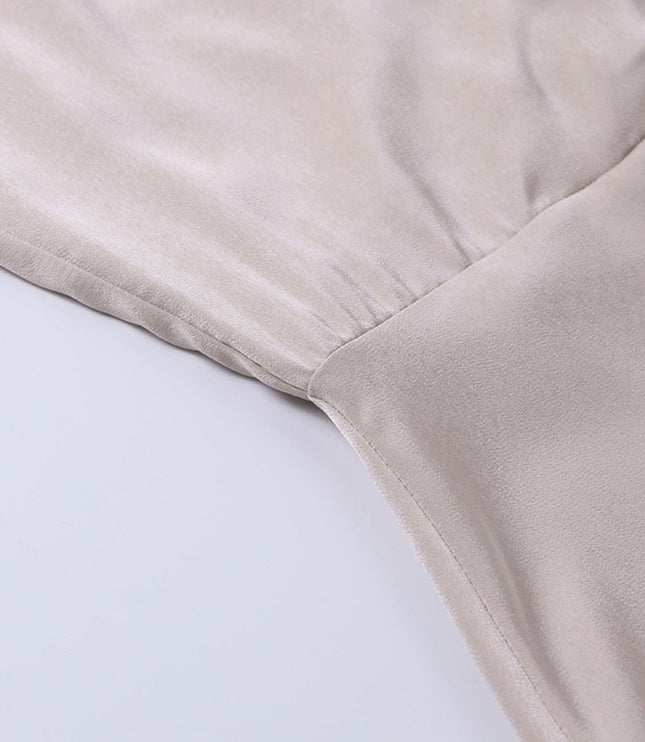 Close-up of the gathered waist seam detail on a beige V-neck maxi slip dress, showing the smooth fabric.