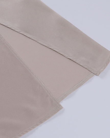 Detailed view of the side slit on the hem of a beige women's maxi slip dress, showing the neat stitching.