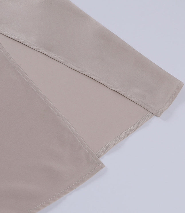 Detailed view of the side slit on the hem of a beige women's maxi slip dress, showing the neat stitching.