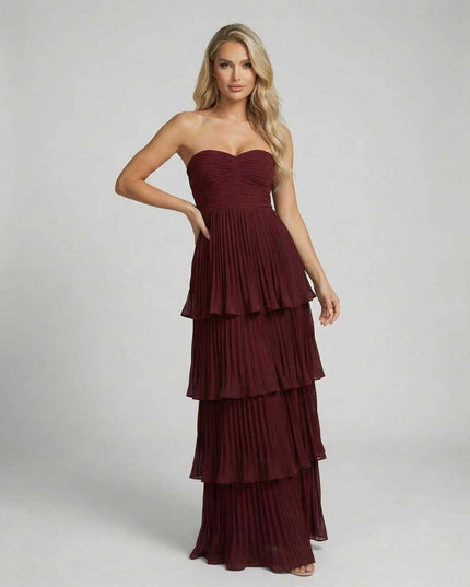 Front view of burgundy strapless wedding guest maxi dress with layered pleated skirt