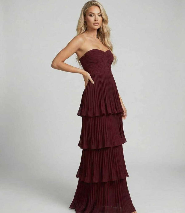 Side view of burgundy strapless maxi dress with pleated layers and flowy skirt
